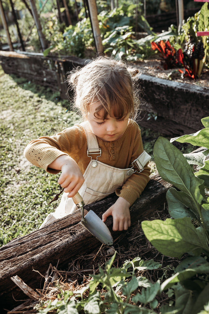 Child playing in the veggie patch with a gardening trowel