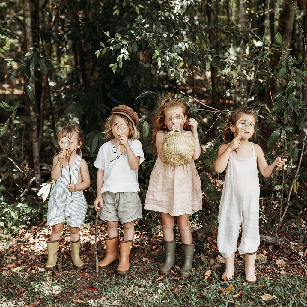 Four kids in forest exploring with magnifying glasses and natural woven basket