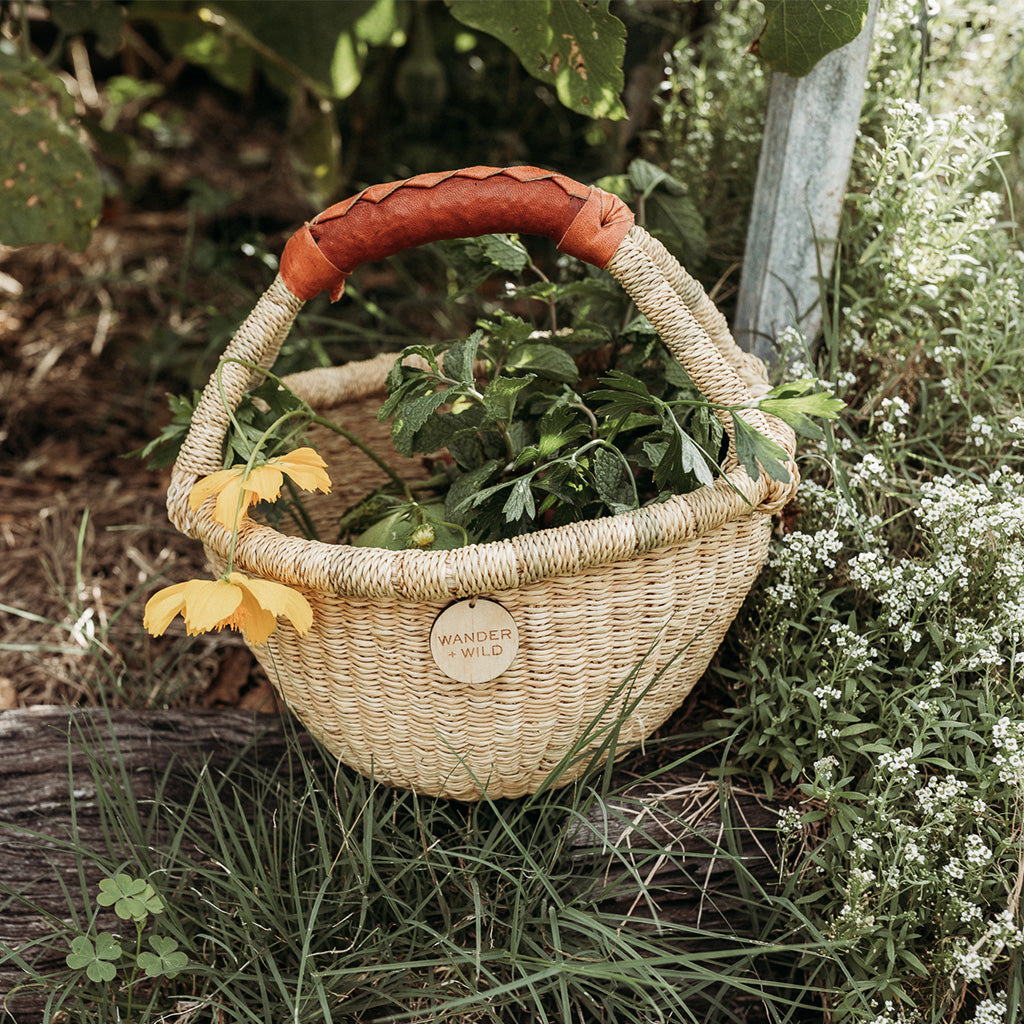 Children's woven basket with tan handle filled with vegetables in the garden