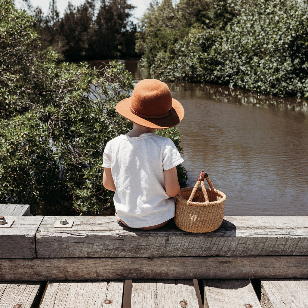Little boy sitting with kid's woven basket while exploring in nature
