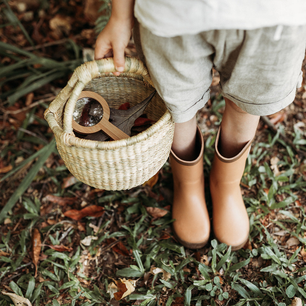Child wearing gumboots holding woven basket filled with a magnifying glass
